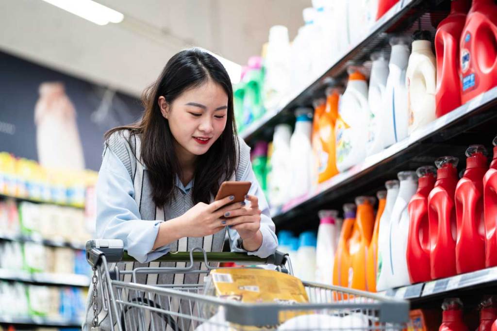 Asian woman looking at mobile pushing shopping cart